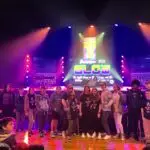 A group of NEUMC youth members, with Revolution 2024 shirts on, pose for a picture in front of the stage at Township Auditorium