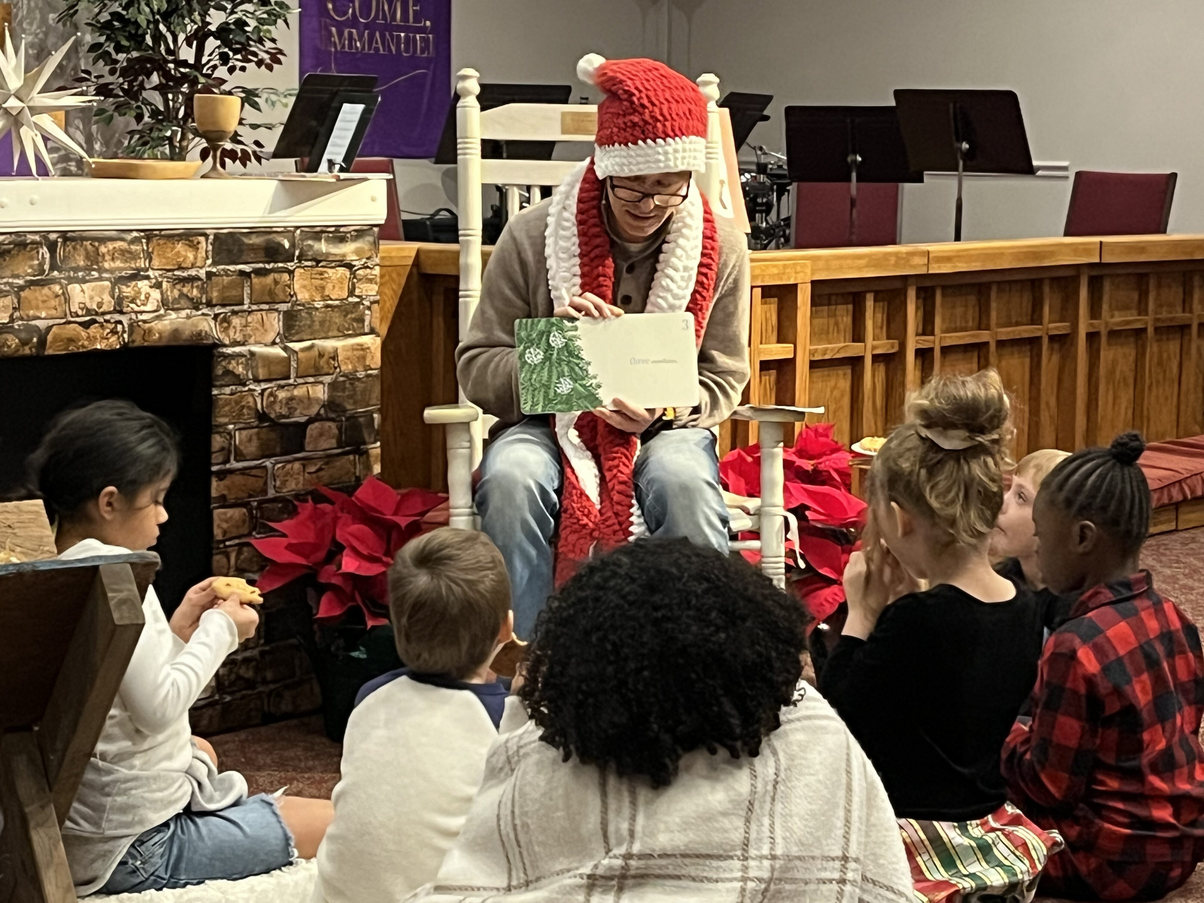 Weston, dressed in a knitted shawl and Santa hat, reads to a group of children