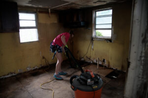 A picture of a 2024 salkehatchie volunteer using a shop vacuum to clean a room.