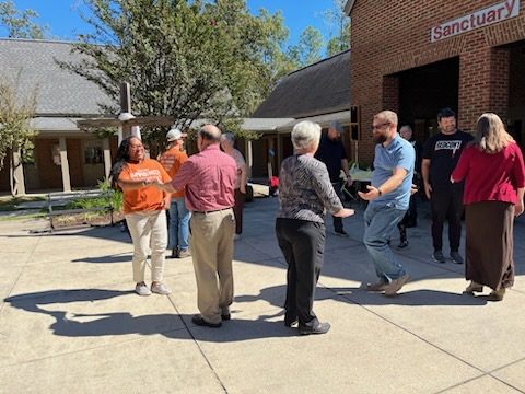 Several adults stand and talk with each other in front of the sanctuary building.