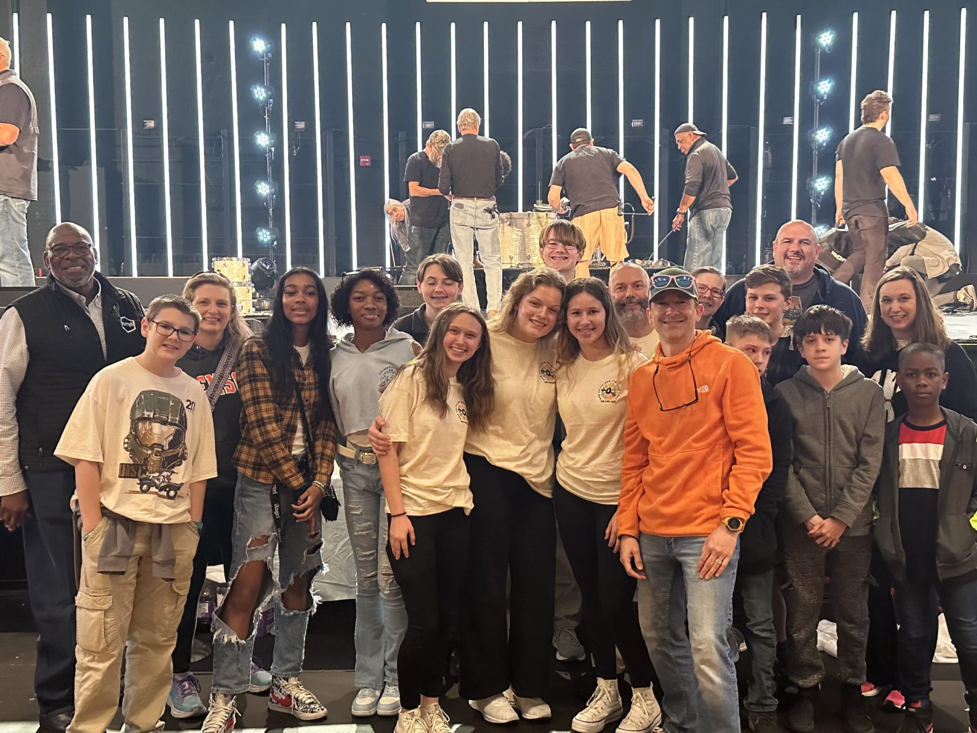 A group of NEUMC youth members, with Revolution 2023 shirts on, pose for a picture in front of the stage at Township Auditorium