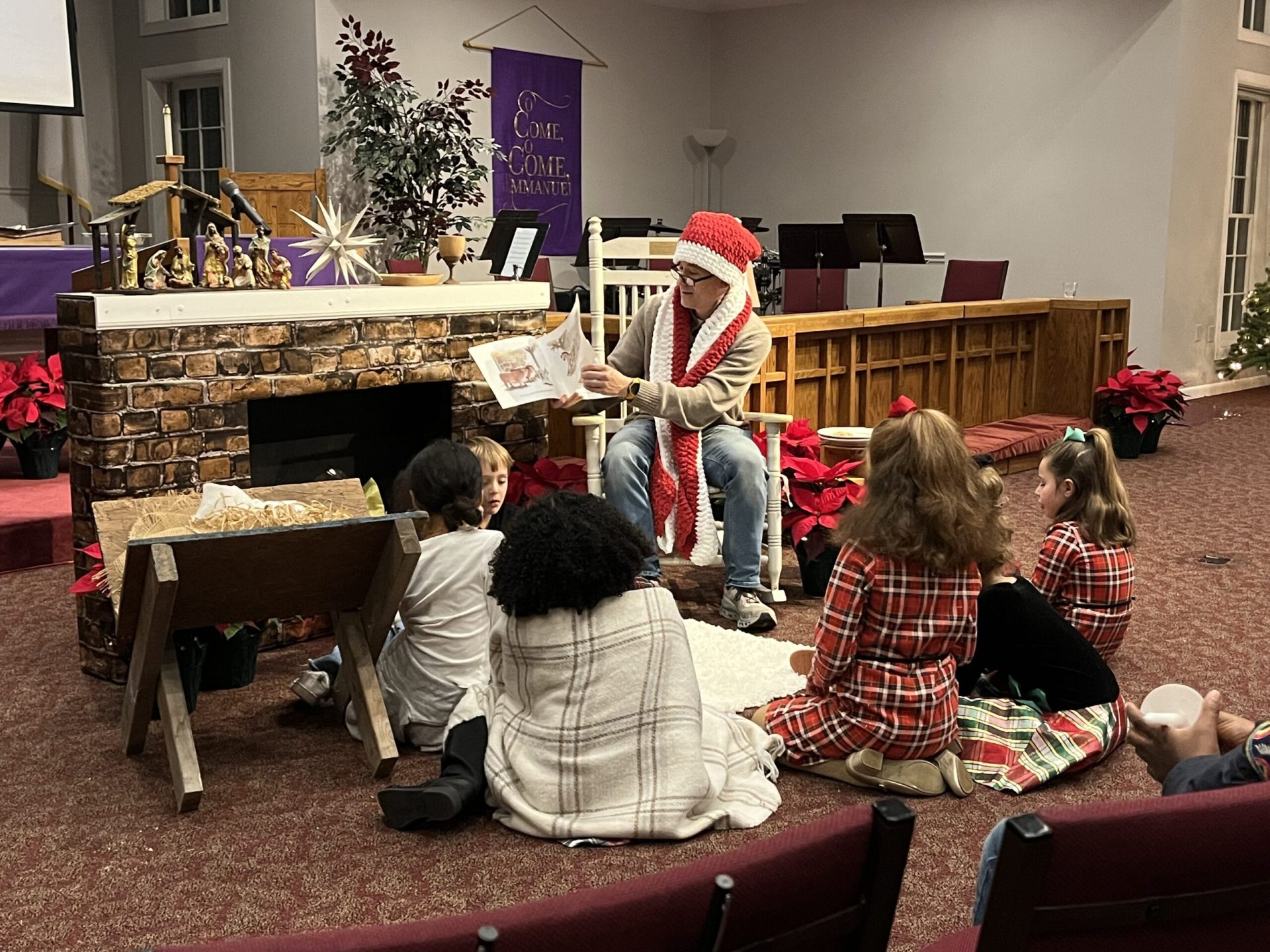 Weston, dressed in a knitted shawl and Santa hat, reads to a group of children